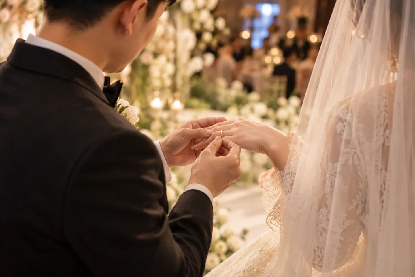 Chú rể đeo nhẫn vào ngón áp út tay trái cô dâu trên sân khấu tiệc cưới